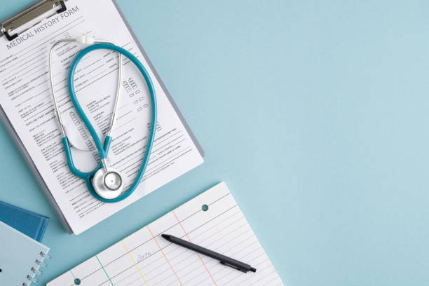 Top view of medical history form in clipboard, folded stethoscope, notebooks and pen on blank card with copyspace on the right